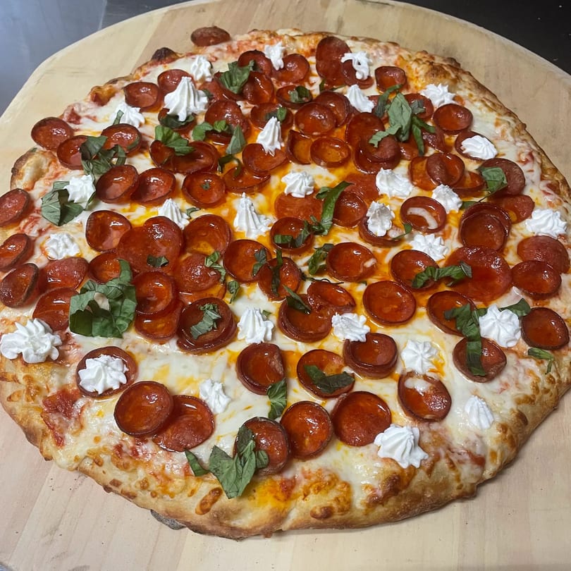 TopCrust Jupiter Kitchen pepperoni pizza with dollops of ricotta cheese and fresh basil on a wooden peel.